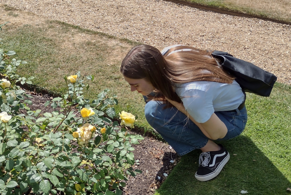 Emma Beniston crouched smelling yellow roses