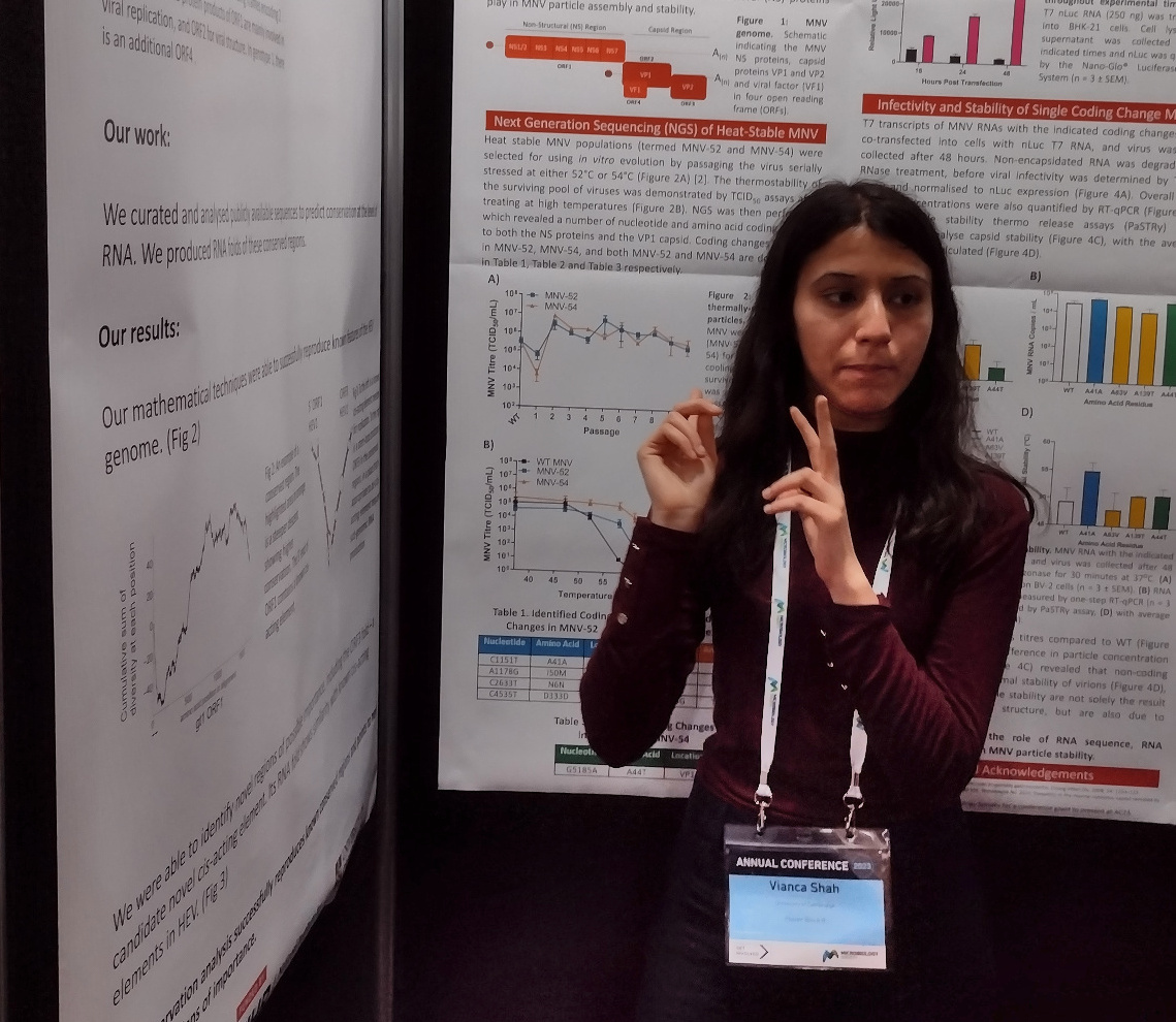 Vianca Shah standing in front of a poster, gesturing, at the 2023 Microbiology Society conference